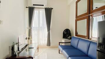 A living room with a blue sofa, a glass coffee table, a small side table, a black fan, and a large mirror.