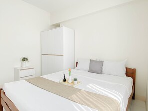A neatly arranged hotel room with a bed, a wardrobe, a bedside table, and a small potted plant. - Comfortable And Trendy 2Br At Apartment Podomoro Golf View (Gunung Putri)