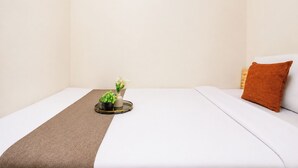 A neatly made bed with a brown throw, a small potted plant, and a vase with white flowers on a bedside table. - Warm And Homey 2Br Apartment Podomoro Golf View (Depok)