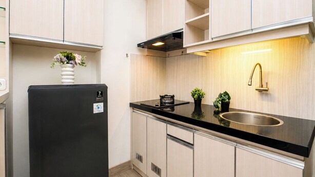 A modern kitchen with light wood cabinets, a black refrigerator, a stainless steel sink, and a built-in oven. - Warm And Homey 2Br Apartment Podomoro Golf View (Depok)