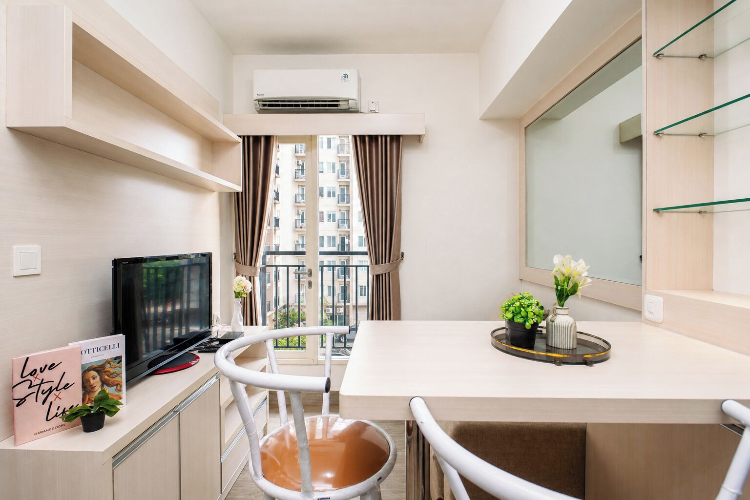 Un espacio habitable compacto con kitchenette, comedor, televisor y balcón con vistas a la ciudad.
