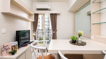 Un espacio habitable compacto con kitchenette, comedor, televisor y balcón con vistas a la ciudad.