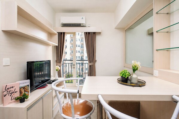 En kompakt bolig med tekøkken, spiseplads, TV og en balkon med udsigt over byen.