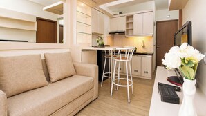 A compact living space with a sofa, a dining area with stools, a kitchen with cabinets, and a small table with a vase of flowers. - Warm And Homey 2Br Apartment Podomoro Golf View (Depok)