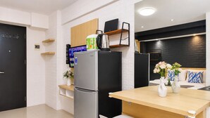 A modern kitchen with a refrigerator, a coffee maker, and a television on a wooden shelf. - Good Warm Studio Room At Apartment Kebagusan City (Jakarta)