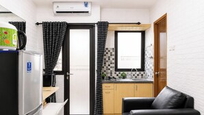A compact kitchen with a refrigerator, a sink, and a dining area with a chair. - Good Warm Studio Room At Apartment Kebagusan City (Jakarta)