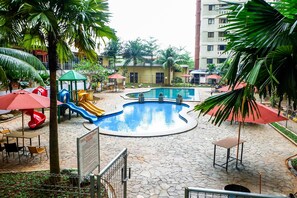 A swimming pool surrounded by palm trees and a playground with slides. - Good Warm Studio Room At Apartment Kebagusan City (Jakarta)