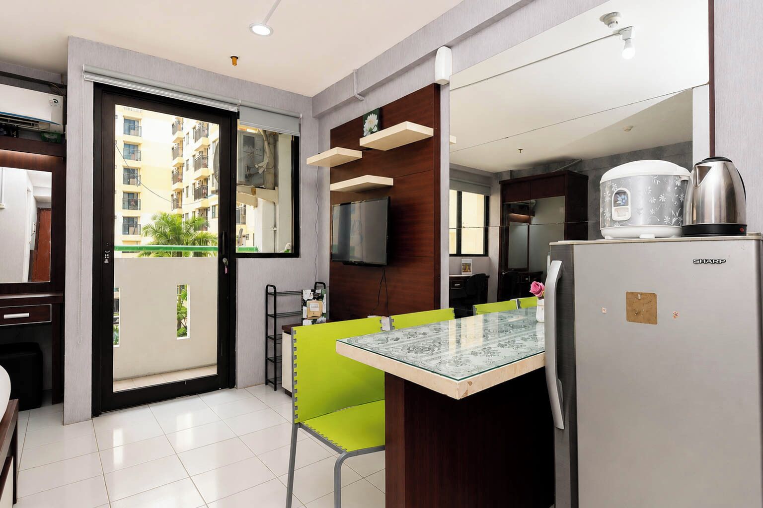 Una cocina moderna con una mesa de vidrio, un refrigerador Sharp y vistas a un área residencial.