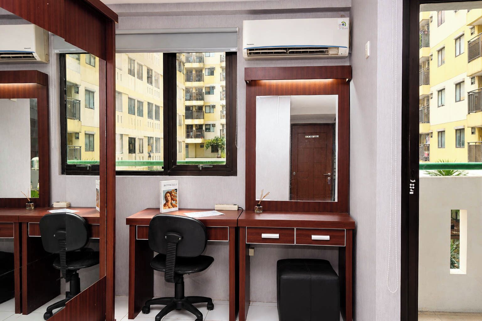 Una habitación con un escritorio de madera, dos sillas de oficina negras, un espejo grande y un equipo de aire acondicionado.