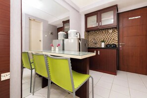 A compact kitchen with a dining area, featuring a glass-top table, green chairs, and wooden cabinets. - Strategic Location Studio At Apartment Kebagusan City (Jakarta)