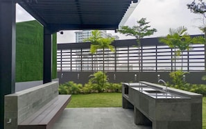 Eine moderne Außenpatio mit einem Betonsink, einer kleinen Gartenanlage und Blick auf eine Stadtlandschaft durch einen Metallzaun.