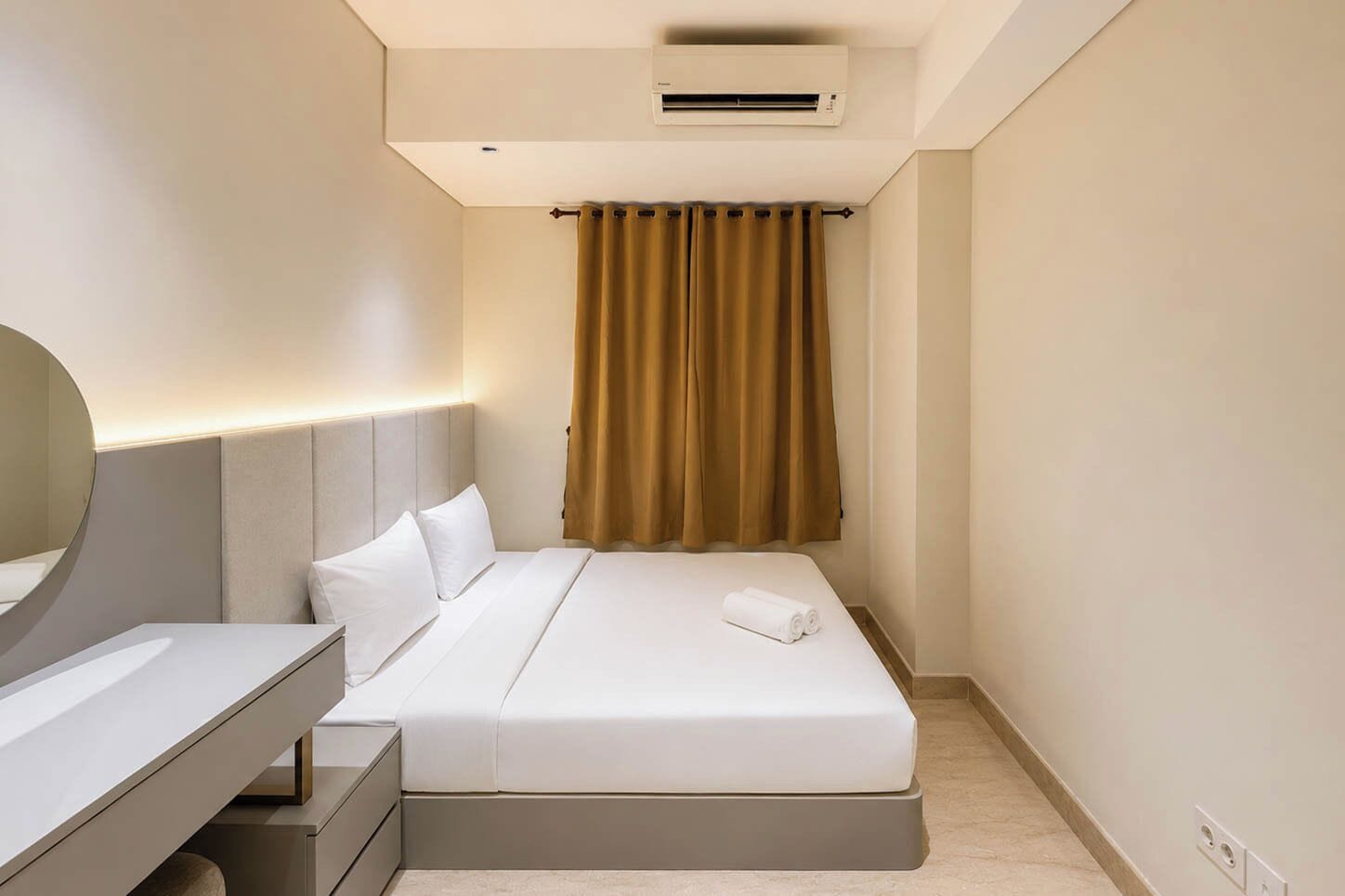 A hotel room with a bed, bedside table, mirror, and an air conditioning unit.
