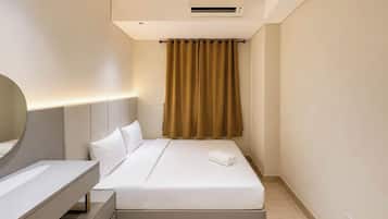 A hotel room with a bed, bedside table, mirror, and an air conditioning unit.