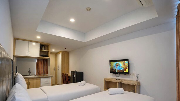 A hotel room with two beds, a TV, a kitchenette, and a ceiling light. - Warm Stay In Studio Room At Apartment De Prima (Medan)