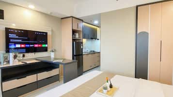 Una habitación de hotel moderna con cama, mesita de noche, televisión, kitchenette y armario.