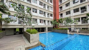 A multi-story residential building with a swimming pool, balconies, and surrounding greenery. - Warm And Comfy Studio At Apartment Lrt City Jatibening (Bekasi)
