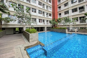 A multi-story residential building with a swimming pool, balconies, and surrounding greenery. - Warm And Comfy Studio At Apartment Lrt City Jatibening (Bekasi)
