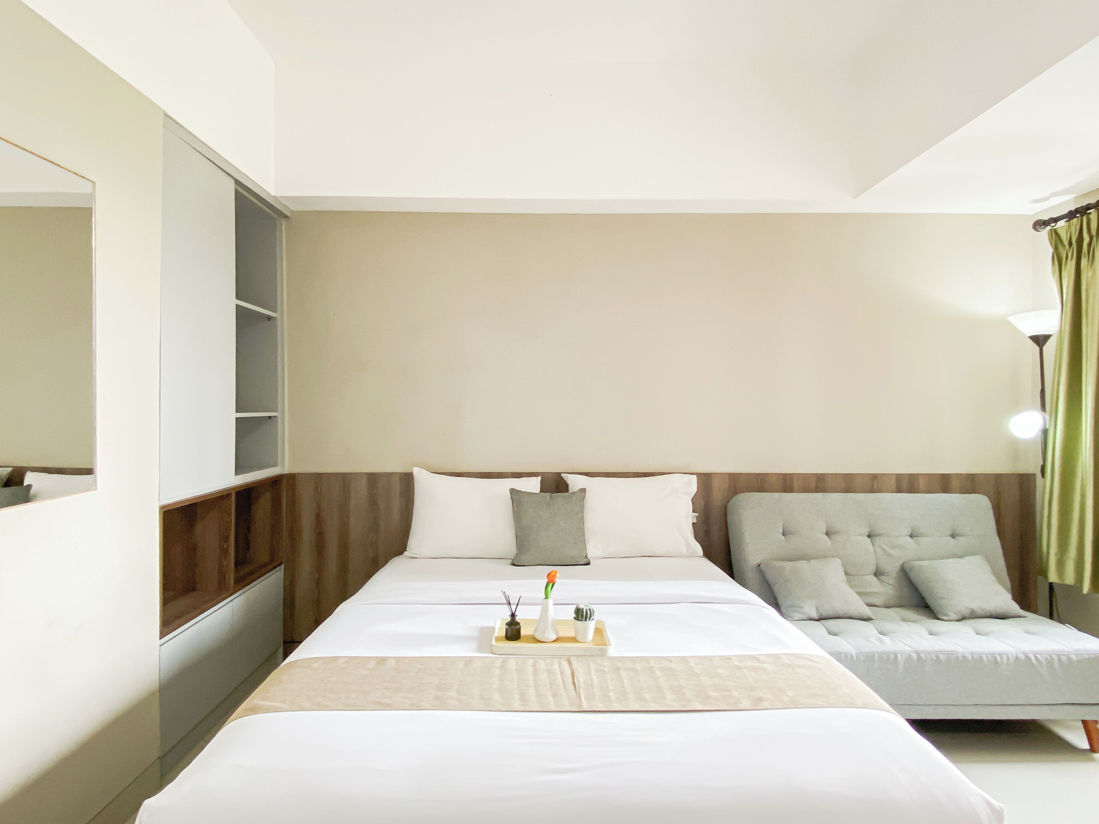 A hotel room with a bed, a sofa, a bedside table, a mirror, and a lamp.