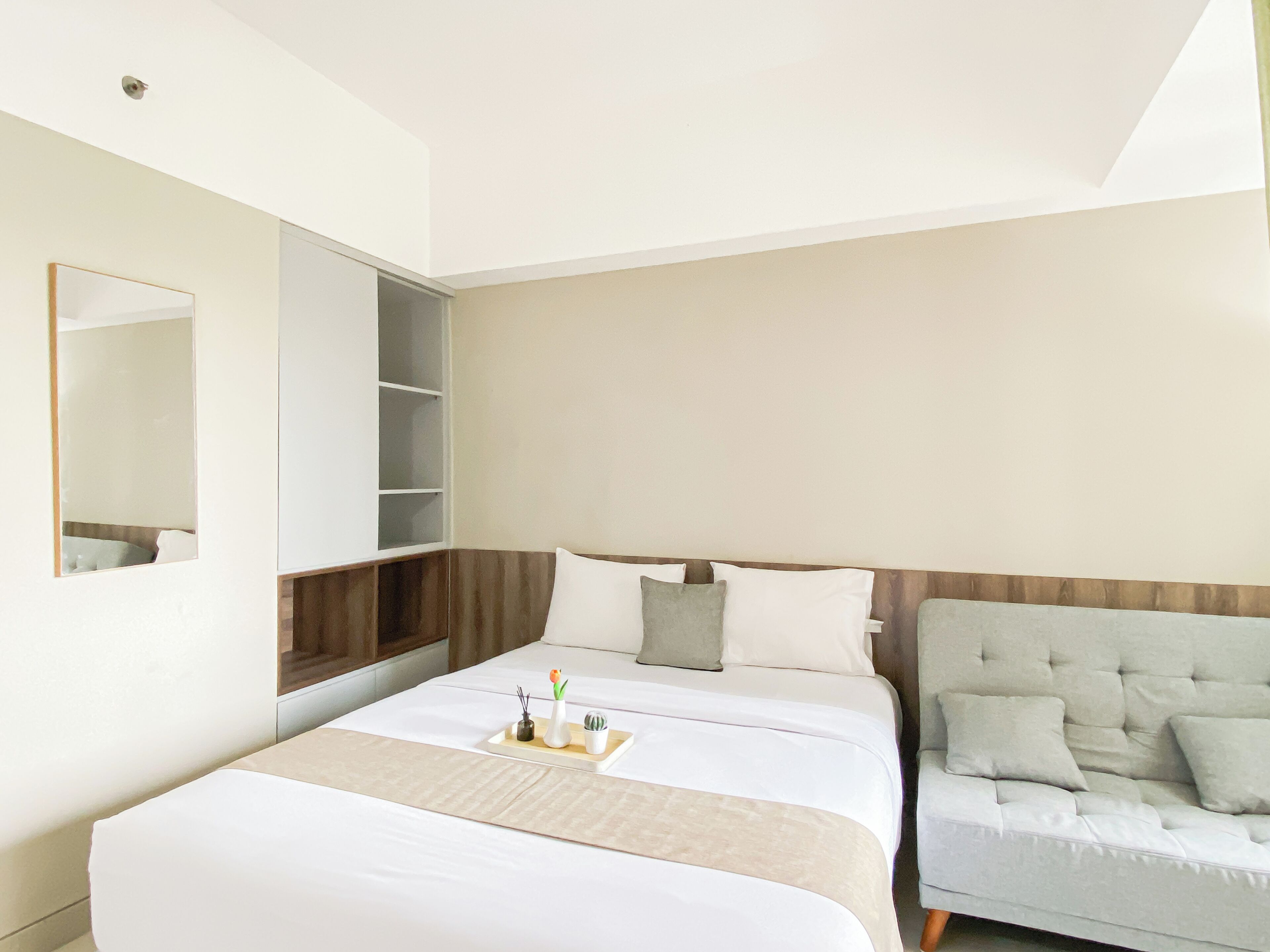 A modern hotel room with a large bed, a seating area with a sofa, a built-in wardrobe, and a large mirror.