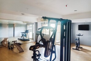 Ein geräumiges Zimmer mit einem großen Spiegel, Trainingsgeräten wie Laufband, Crosstrainer und Gewichten sowie einem an der Wand montierten Fernseher.