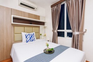 A hotel room with a bed, a bedside table, a window with curtains, a wall-mounted air conditioner, and a headboard. - Cozy Living 2Br Apartment At Cinere Bellevue Suites (Depok)