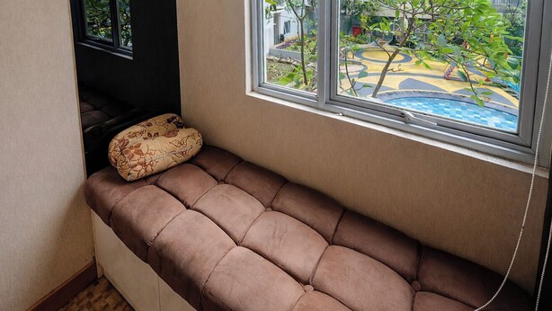 A room with a built-in bench, a window with a view of a pool and greenery, and a wall-mounted telephone. - Warm Combined 3Br At Maple Park Sunter Apartment (Jakarta)