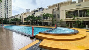 Ein Schwimmbecken mit Whirlpool, umgeben von einer gefliesten Terrasse und einem Gebäude mit Balkonen.