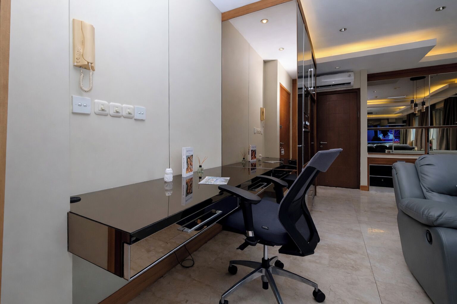 Um espaço de escritório moderno com uma mesa de vidro, cadeiras de escritório, um telefone e uma televisão ao fundo.