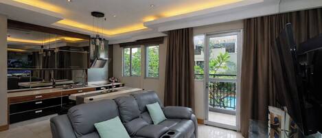 A modern living room with a sofa, a kitchen area, and a balcony with a pool view.