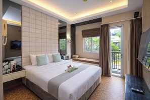 Ein Hotelzimmer mit einem großen Bett, einem Fernseher, einem Nachttisch, einem Fenster mit Vorhängen und einem Balkon.
