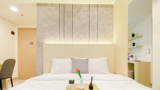 Una habitación de hotel con una cama, una silla, una mesita con una flor y una mesita de noche con una lámpara.