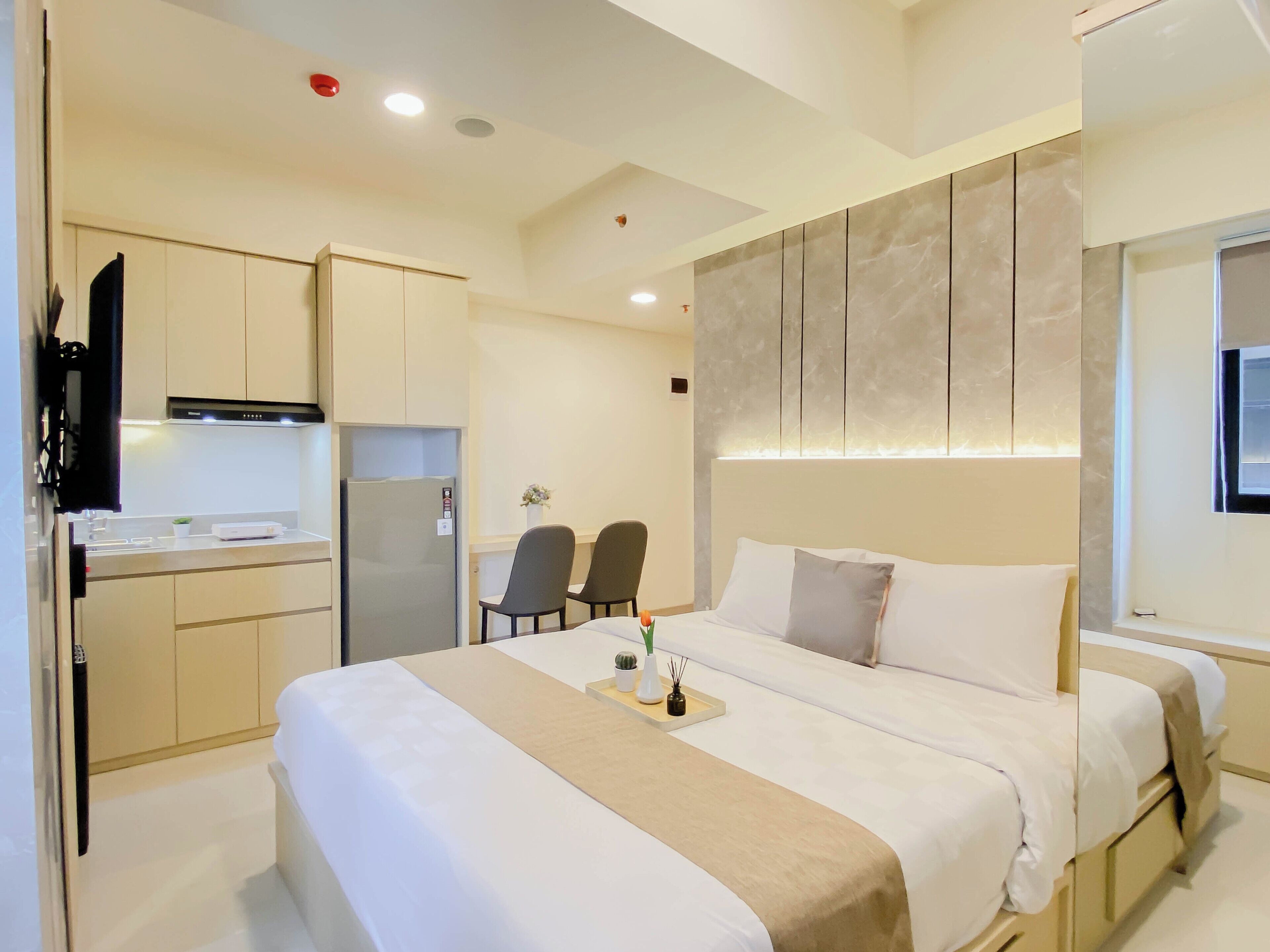 A hotel room with a bed, bedside tables, a desk, a chair, a kitchenette, and a bathroom.