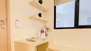 Una habitación con un escritorio blanco, un taburete pequeño, una ventana con vistas y una puerta con picaporte.