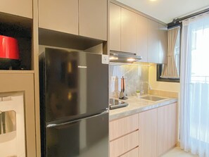 A compact kitchen with a black refrigerator, a sink, and light-colored cabinets. - Homey And Serene 2Br At Apartment Meikarta District 2 (Cikarang)