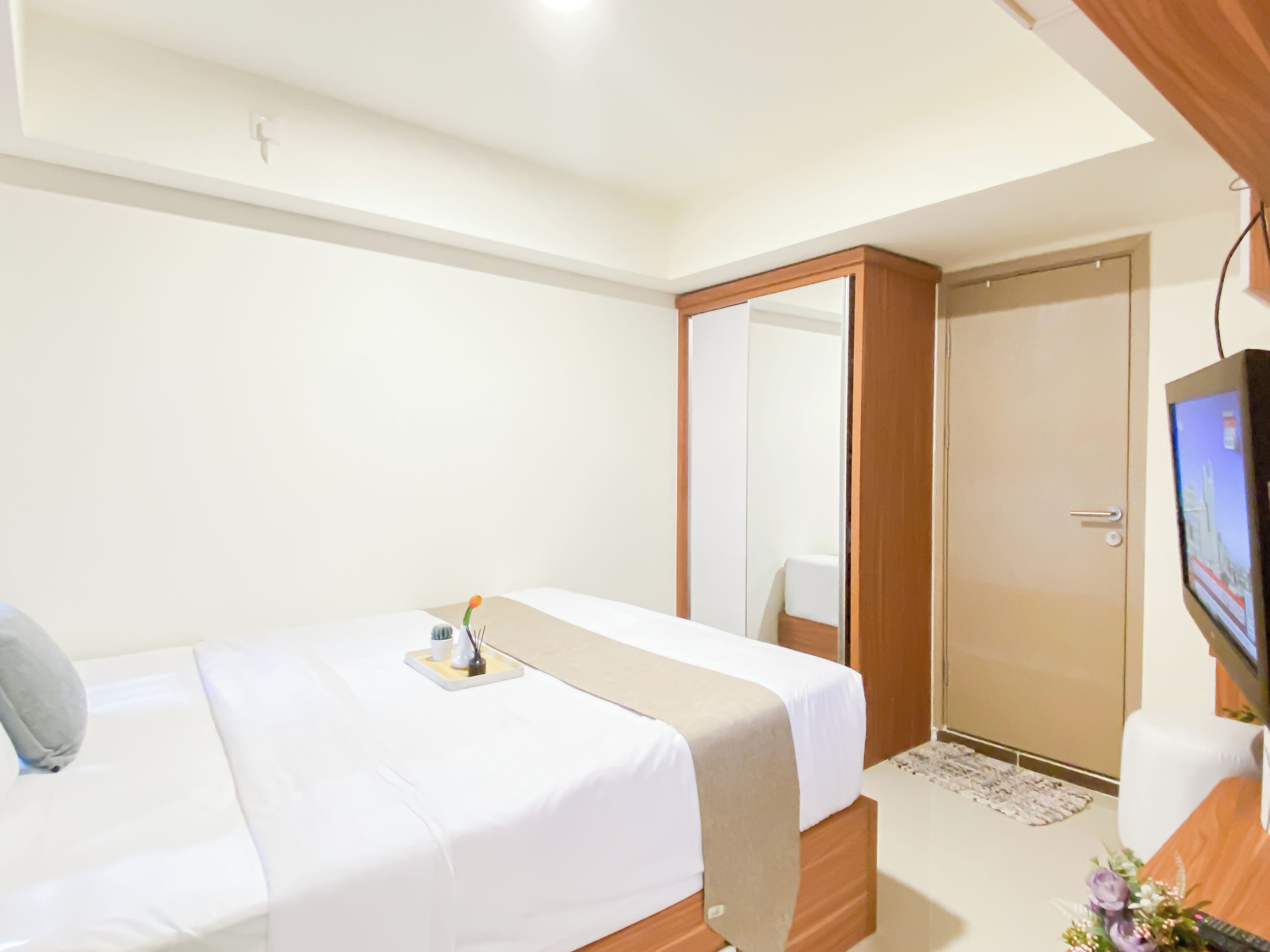 A hotel room with a bed, a television, a wardrobe, and a mirror.