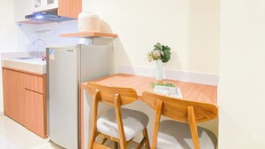 Een compacte keuken met een koelkast, een spoelbak, houten keukenkastjes en een eettafel met twee stoelen.