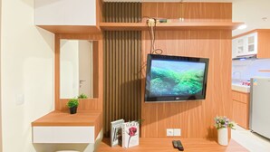 Een moderne badkamer met een houten wastafelmeubel, een spiegel, een aan de muur bevestigde televisie en een kleine plant in pot.