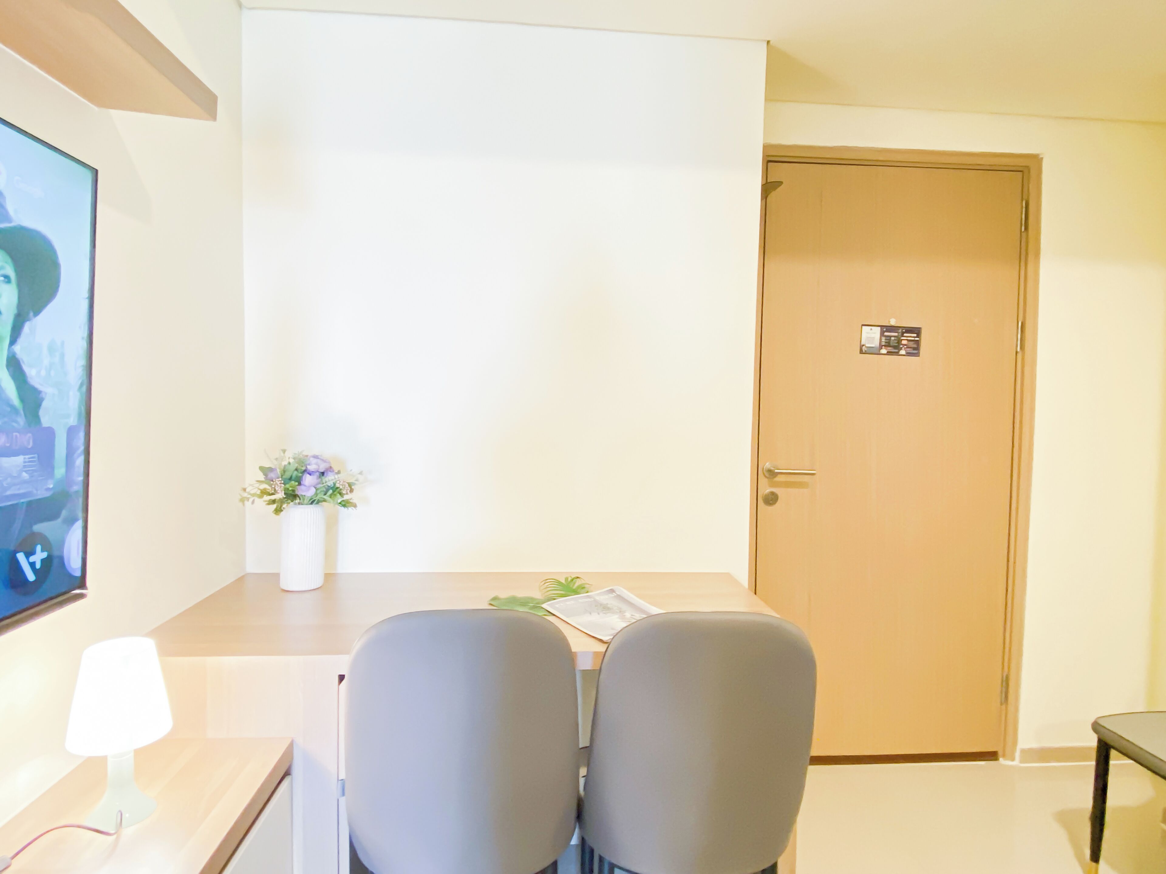 A hotel room with a bed, a bedside table, a lamp, a TV, and a door.