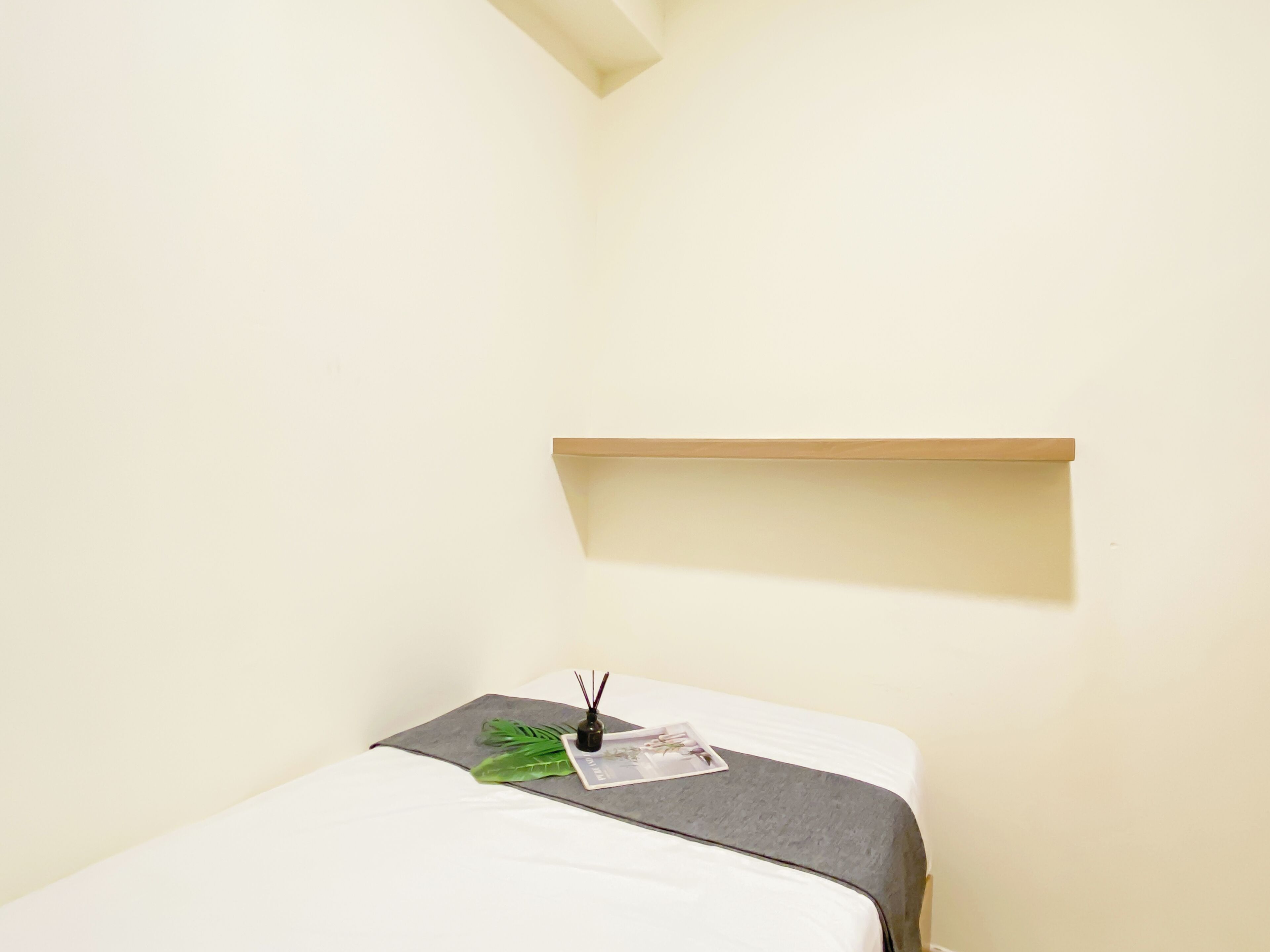 A room with a bed, a small shelf, a magazine, and a decorative item on the bed.