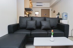 A modern living room with a black leather sofa, a white coffee table, and a single tulip in a white vase. - Cozy Stay 2Br At Apartment Meikarta District 2 (Cikarang)