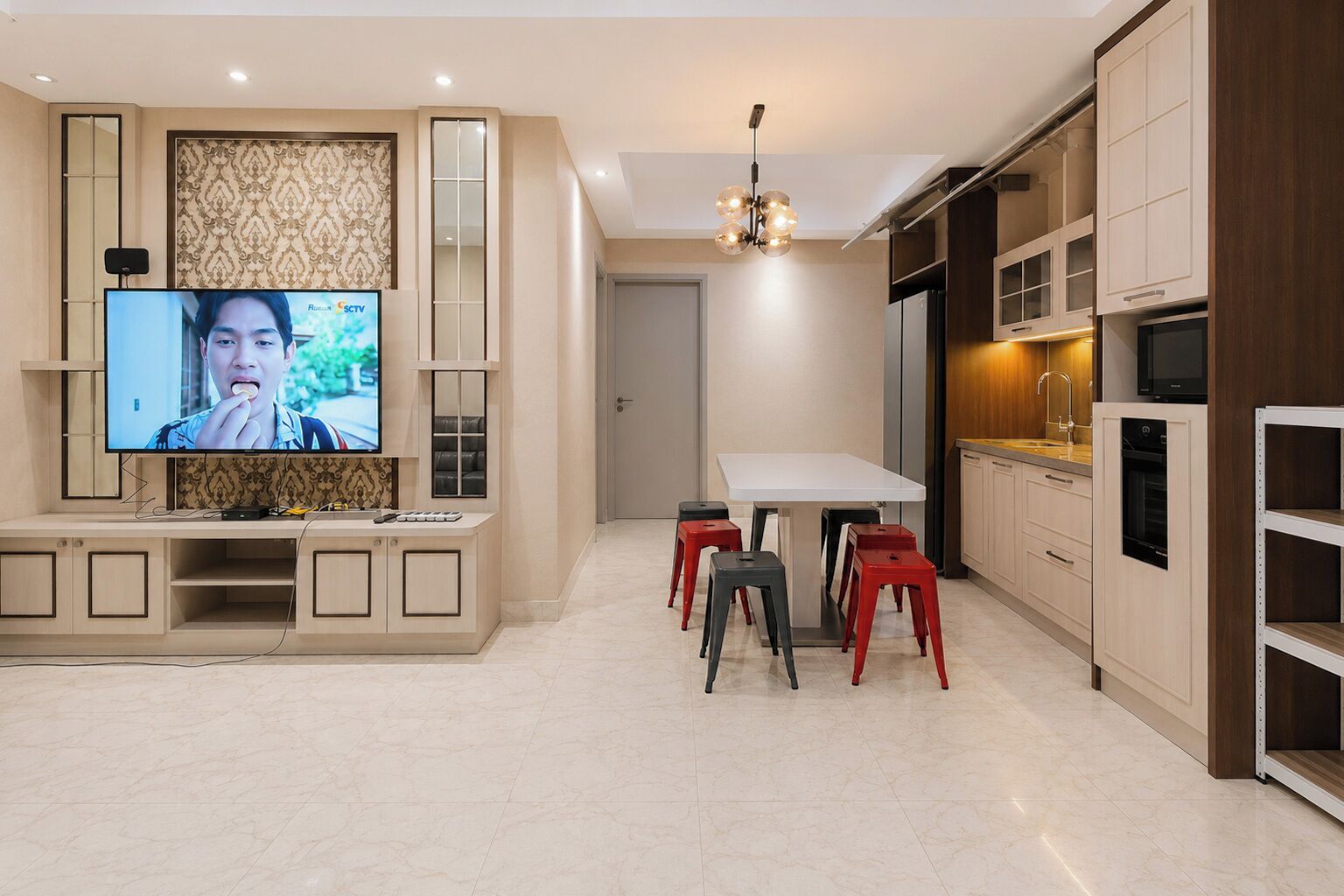 Una cocina moderna con zona de comedor, un televisor montado en un mueble y una lámpara colgante sobre la mesa.