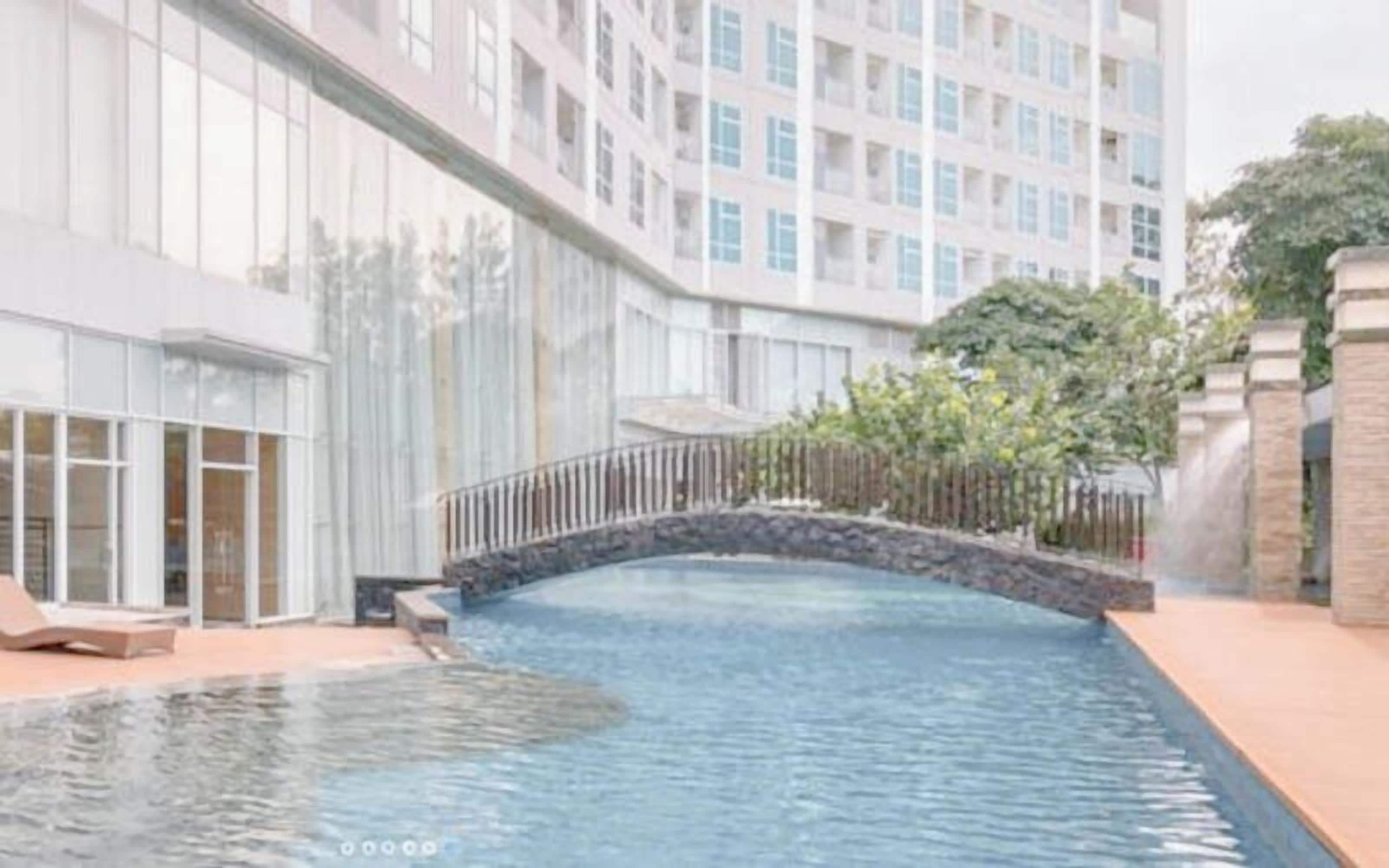A modern hotel with a swimming pool, a stone bridge, and a view of a high-rise building.
