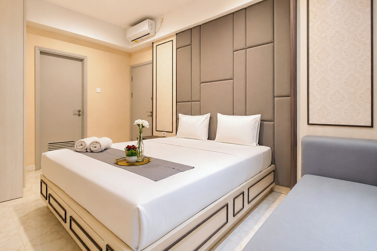 Habitación de hotel con una cama grande, una mesita de noche con un florero y un aire acondicionado de pared.