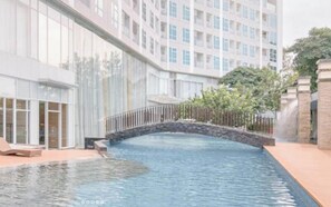 Ein Schwimmbecken mit einer Steinbrücke, umgeben von einem modernen Gebäude mit großen Fenstern und einem gepflegten Garten.
