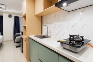 Cocina compacta con estufa a gas, un lavamanos y un reloj en la pared.