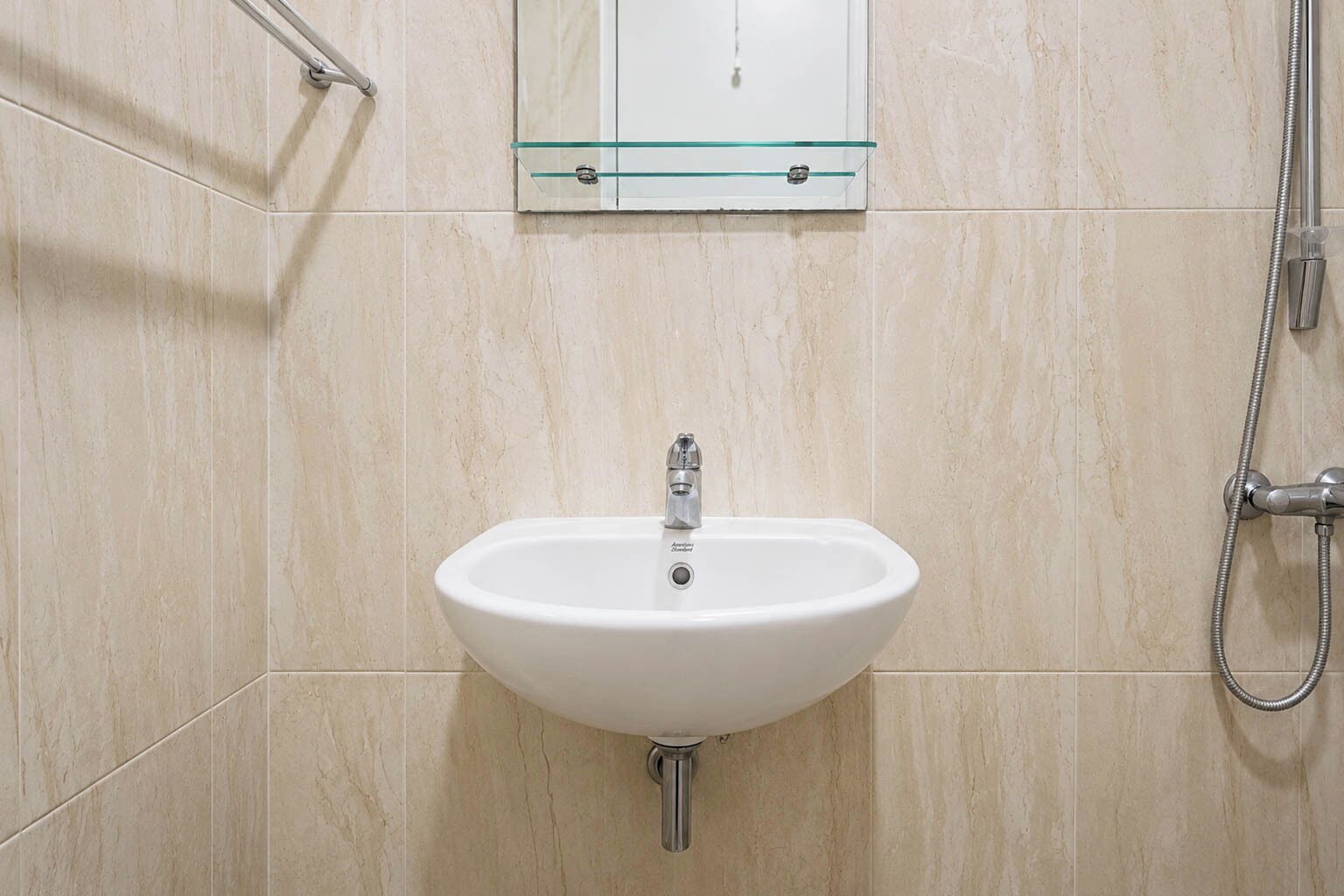 A bathroom with a white sink, a glass cabinet above it, and a showerhead to the right.