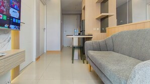 En moderne stue med en grå sofa, et fjernsyn ophængt på væggen og et køkken i baggrunden.