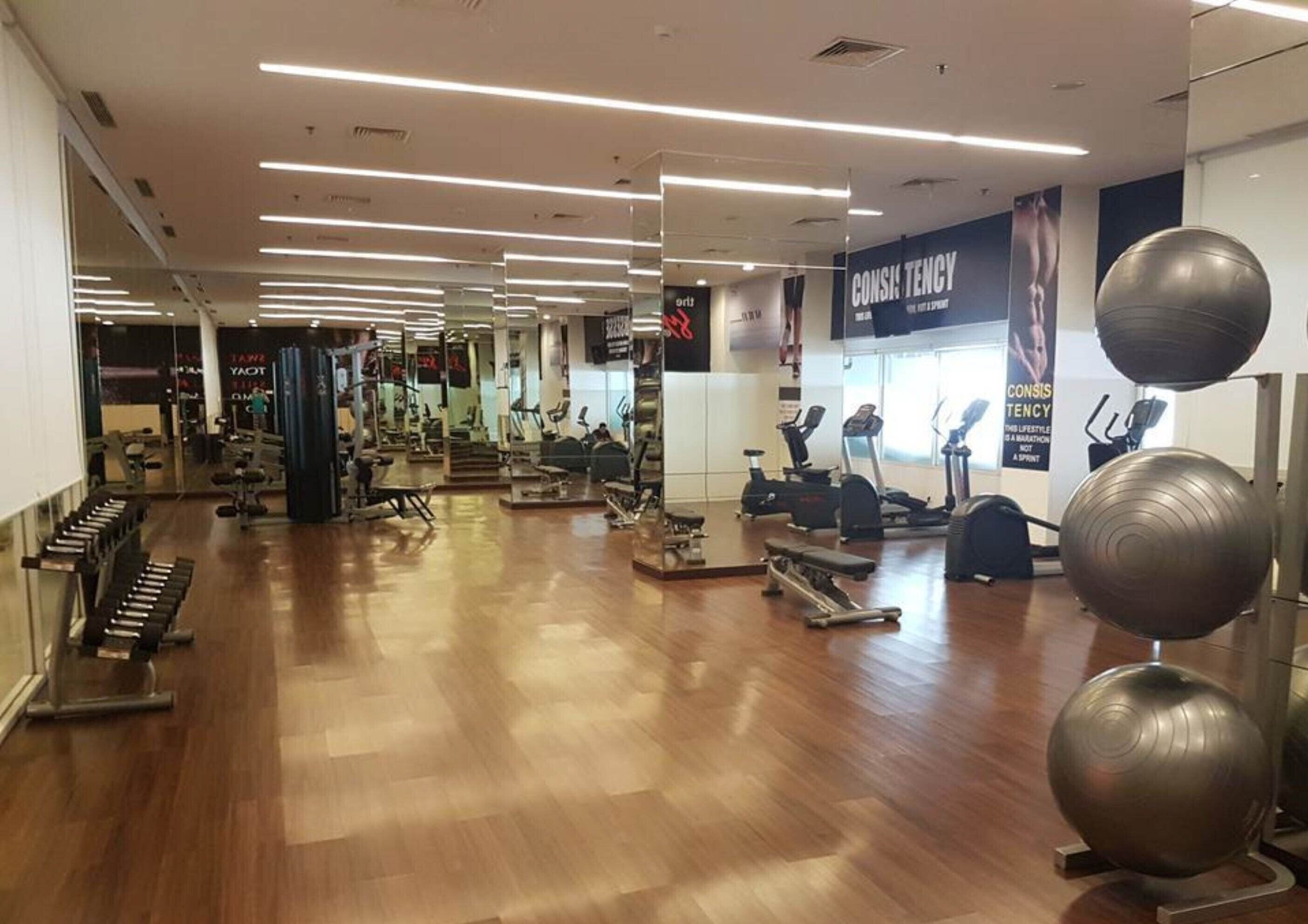 Un gimnasio con equipo de ejercicio diverso, incluyendo cintas de correr, bicicletas estáticas y pesas sueltas.