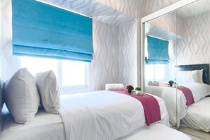 A hotel room with two beds, a large mirror, and a window with blue blinds. - Contemporary Style 2Br Apartment At Tanglin Supermall Mansion (Surabaya)