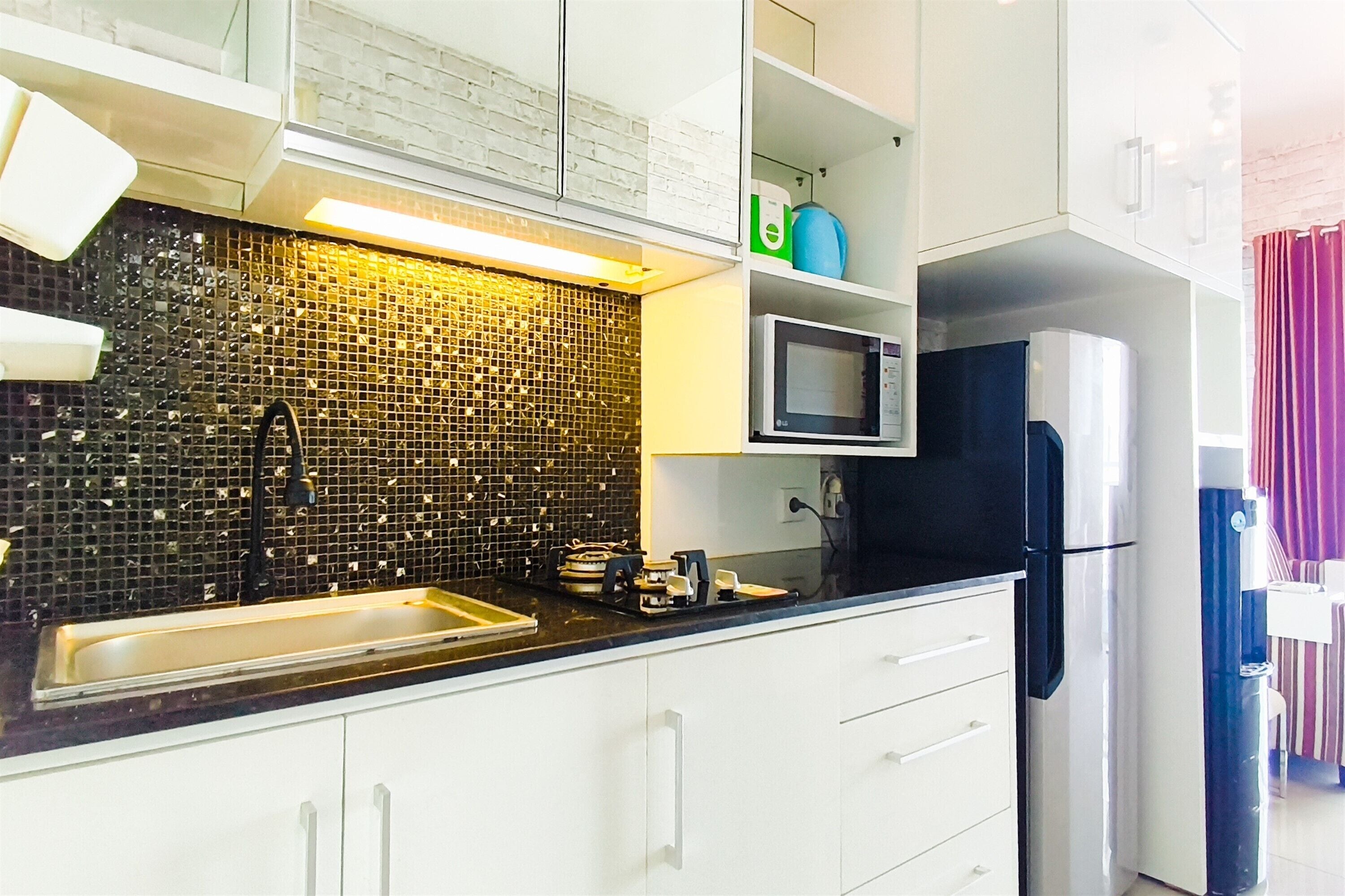 A kitchen with a black tiled backsplash, white cabinets, a microwave, and a refrigerator.